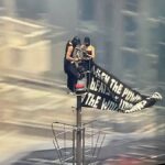 Two people climb to the top of Empire State Building with massive banner