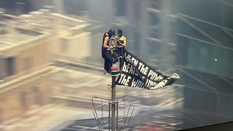 Two people climb to the top of Empire State Building with massive banner